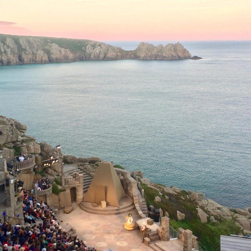 Kayalıkların içine inşa edilmiş bir açık hava tiyatrosu gün batımında denize bakmaktadır. İzleyiciler, arka planda kayalık uçurumlar ve sakin su ile sahnede bir performans izliyor; su sporları tatili ile geçen bir gün için mükemmel bir son.