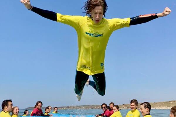 A summer school student leaping from a surfboard into the water.